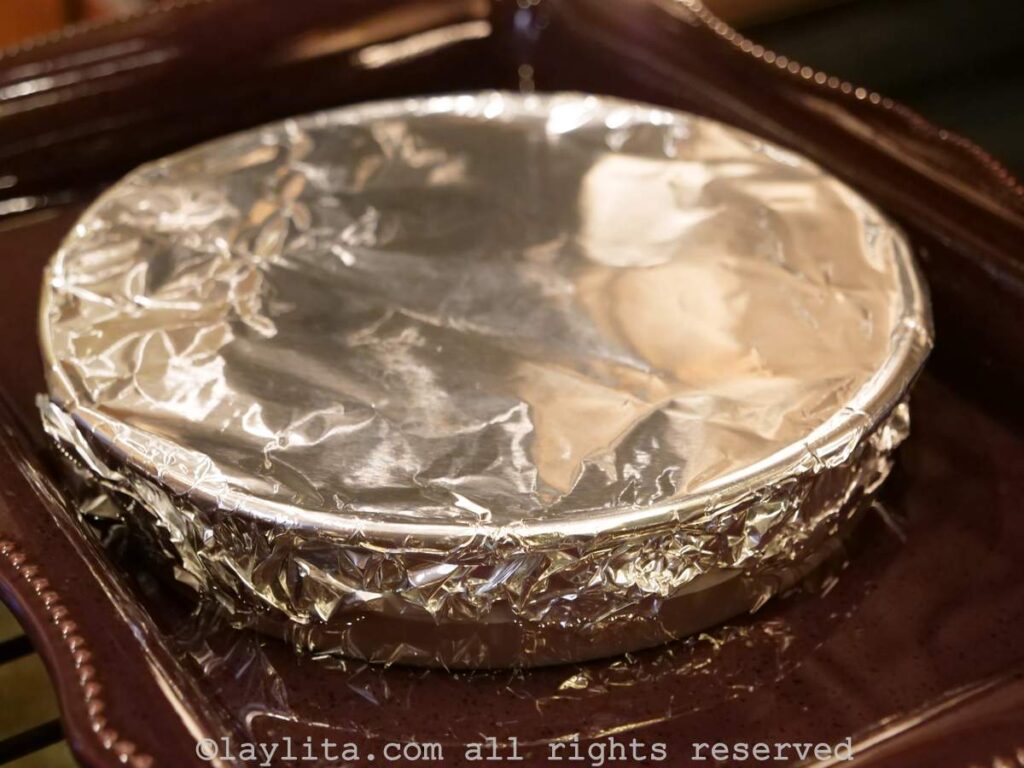 Cake pan covered in foil in a water bath in the oven