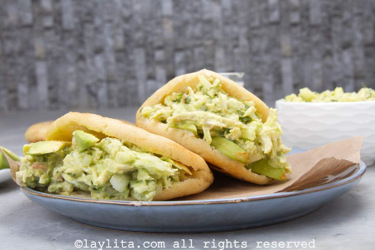 Up close side view of two chicken avocado reina pepiada arepas served on a plate lined with brown paper.