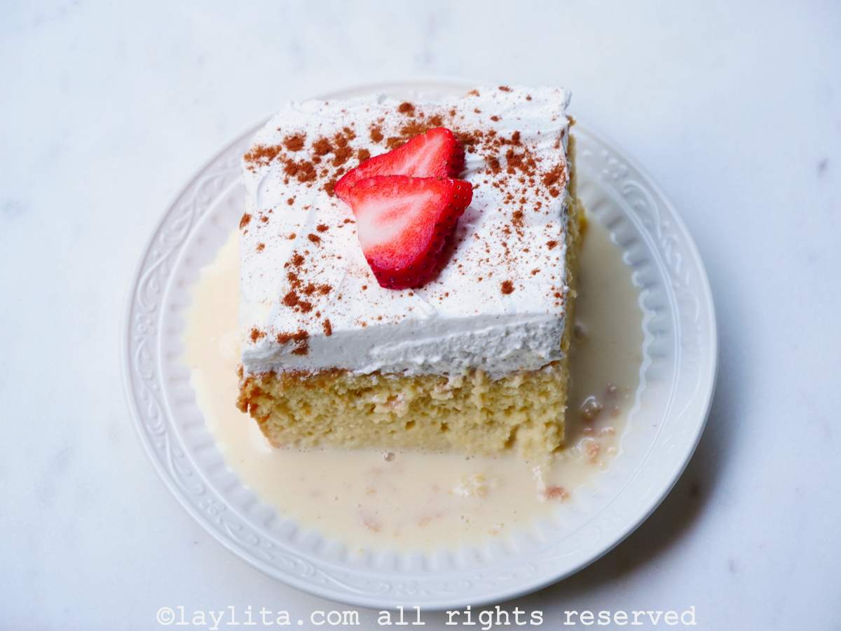 Slice of tres leches cake on a plate with milk mix on the bottom and strawberries on top.