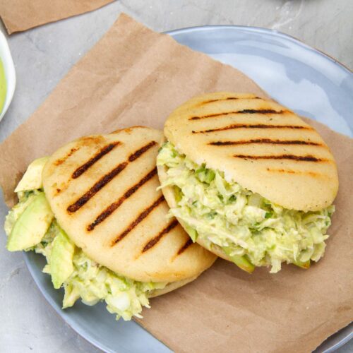 Overhead shot of two Venezuelan chicken avocado stuffed arepas with grill marks on the arepas.