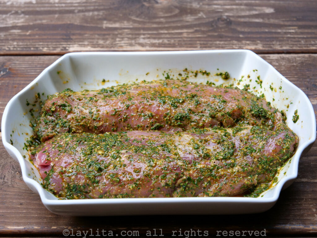 Raw pork tenderloins marinating in herb chimichurri.