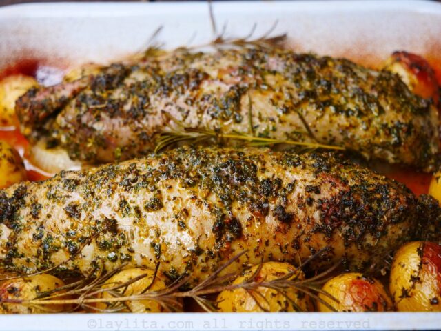 Pork tenderloin coated in chimichurri with potatoes on the side roasting in the oven.