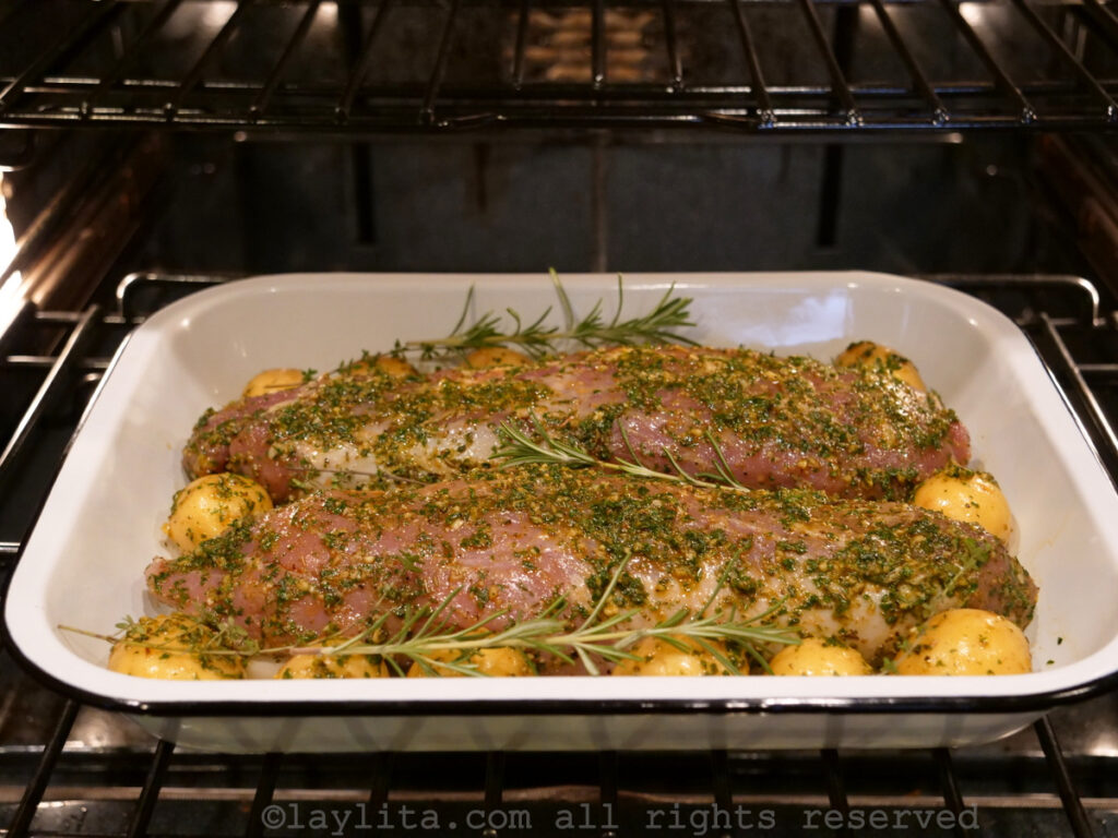 Pork tenderloin coated in chimichurri with potatoes on the side roasting in the oven.