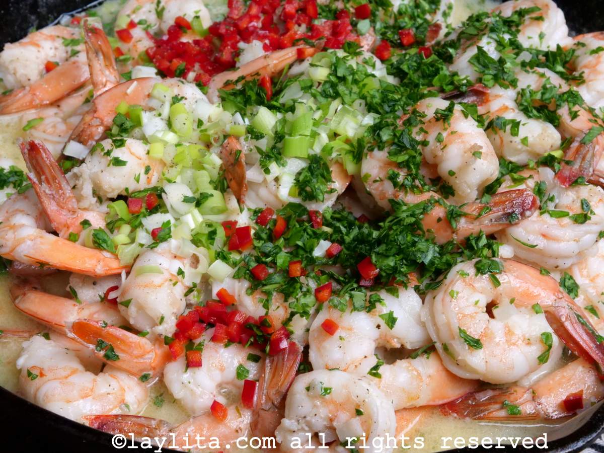 Camarones al ajillo in a skillet topped with parsley, chili and chopped scallions