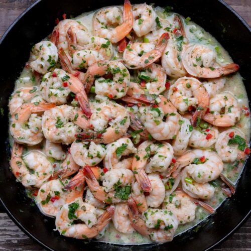 Camarones al ajillo topped with fresh chopped parsley in a skillet
