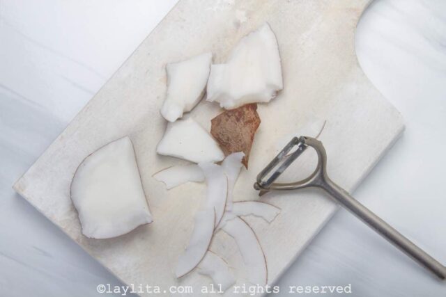 Pieces of fresh coconut on a cutting board with a peeler