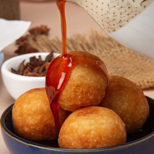 Close up of buñuelos de yuca in a blue bowl with the syrup being poured on top.