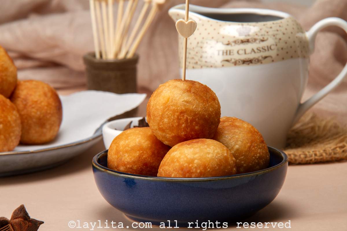 Fried buñuelos de yuca served in a blue bowl with the syrup in the background.