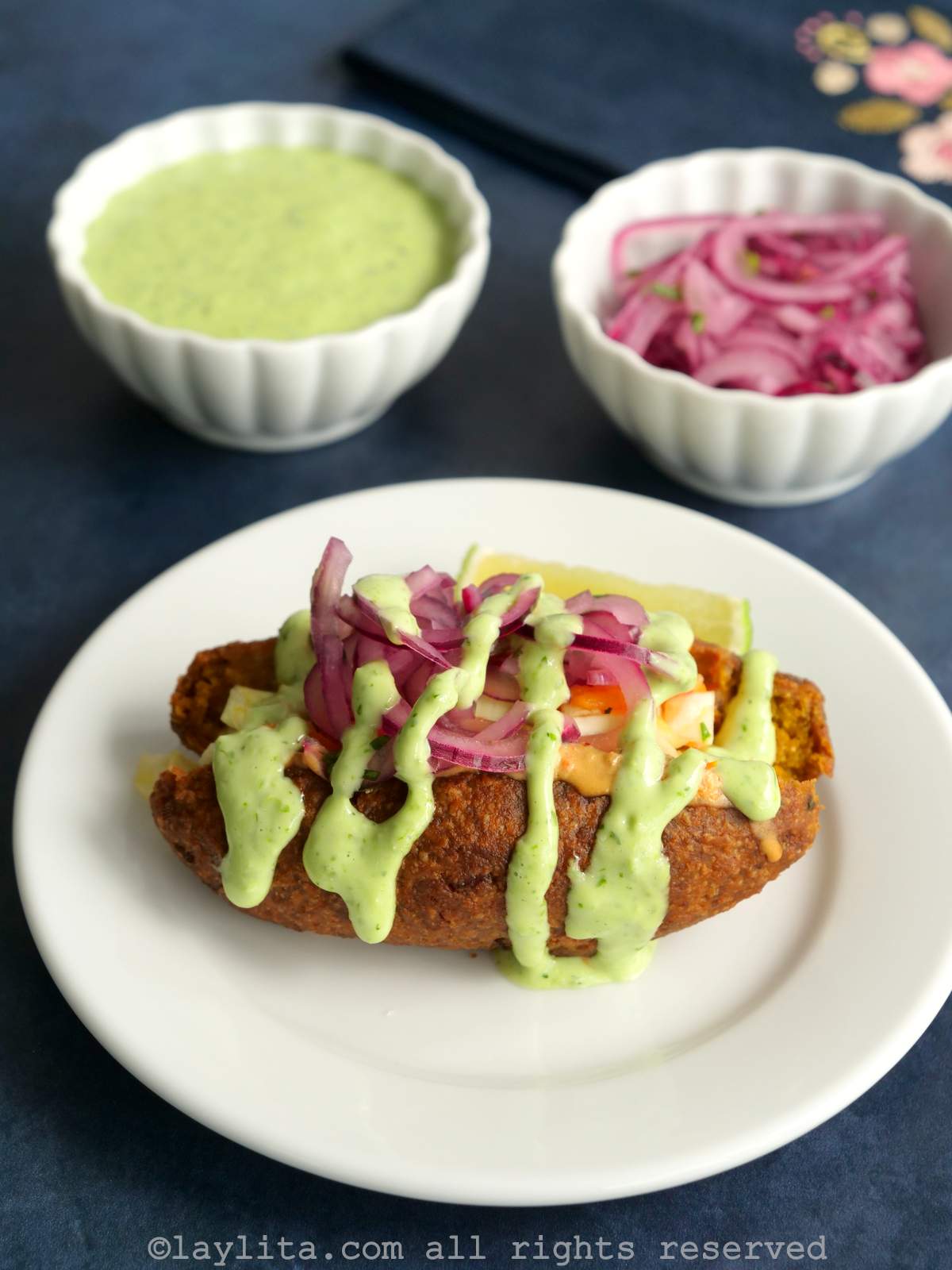 Ecuadorian fish and plantain croquette called corviche on a white plate and topped with green sauce and pickled red onions