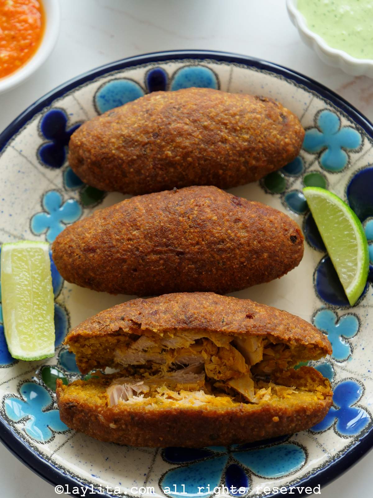 Ecuadorian fish and plantain croquettes called corviches on a white and blue plate with lime wedges on the side