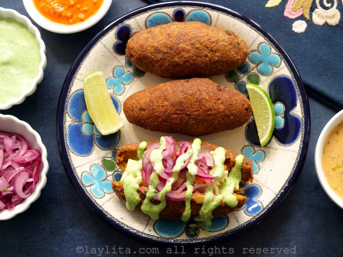 Overhead shot of three corviches on a plate with one cut in half and topped with onions and a green sauce.