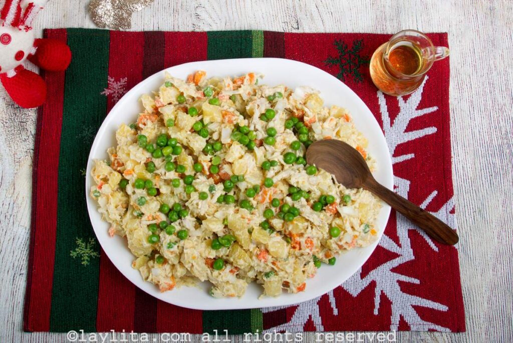 Chicken potato salad served on a white serving platter on a red and green background with a wooden spoon for serving.