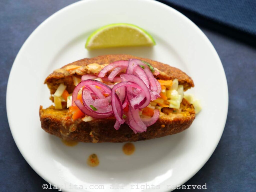 One corviche split in half on a plate with pickled red onions on the top.