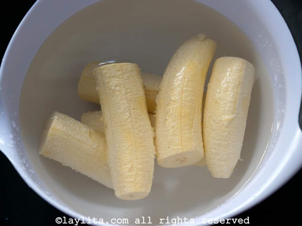 A white bowl with peeled green plantains covered with water