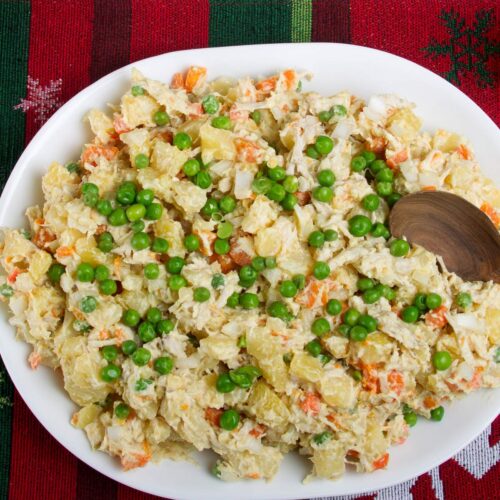 Chicken potato salad served on a white serving platter on a red and green background with a wooden spoon for serving.