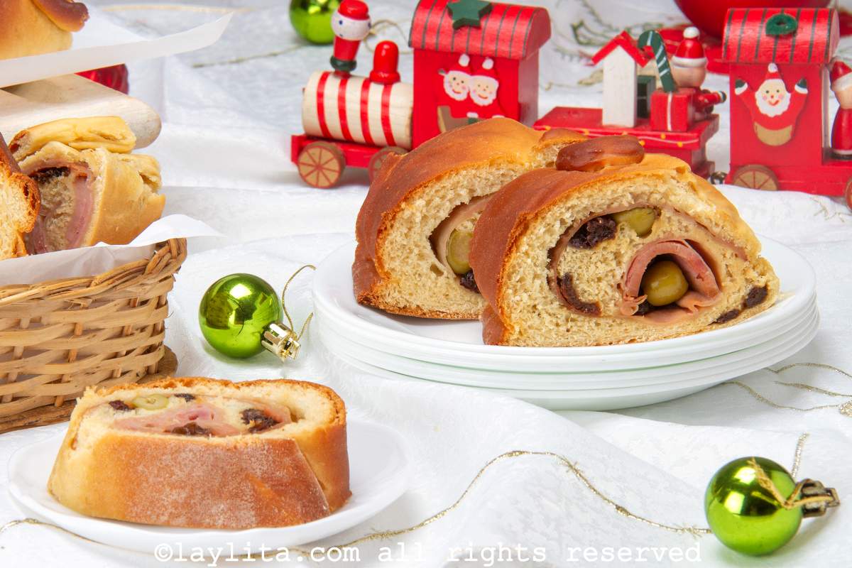 Slice of pan de jamon on a plate with another plate with two slices on it, with a Christmas train in the background.