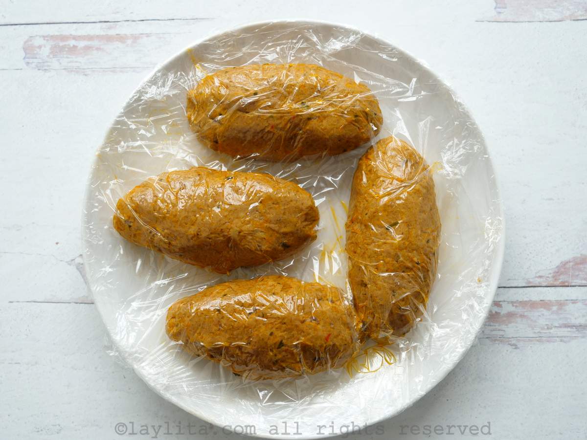 Uncooked corviches covered in plastic wrap on a plate