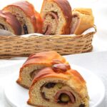 Two slices of pan de jamon on a white plate with more slices in a basket in the background.