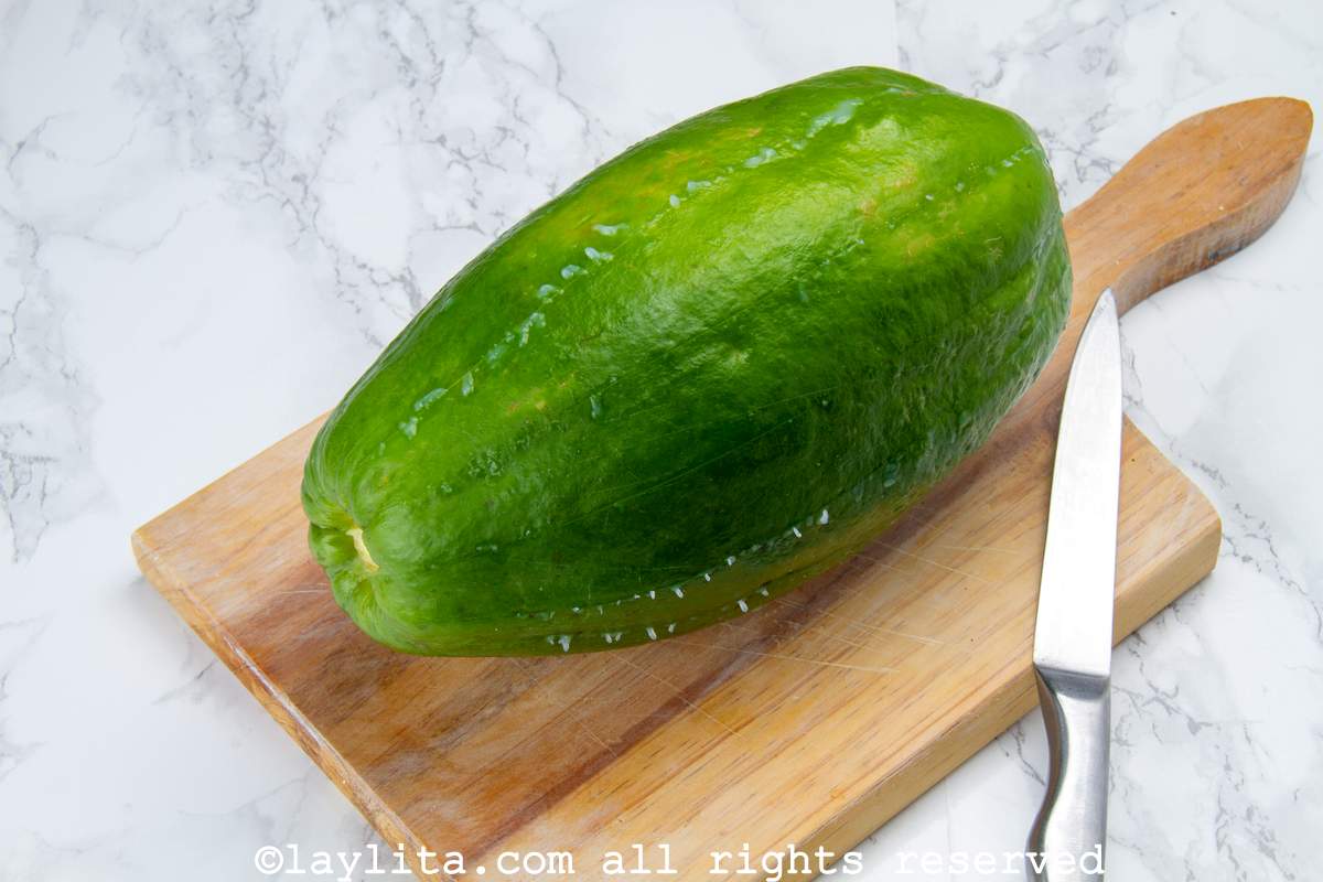 Green papaya on a wooden cutting board with white liquid coming out of it.