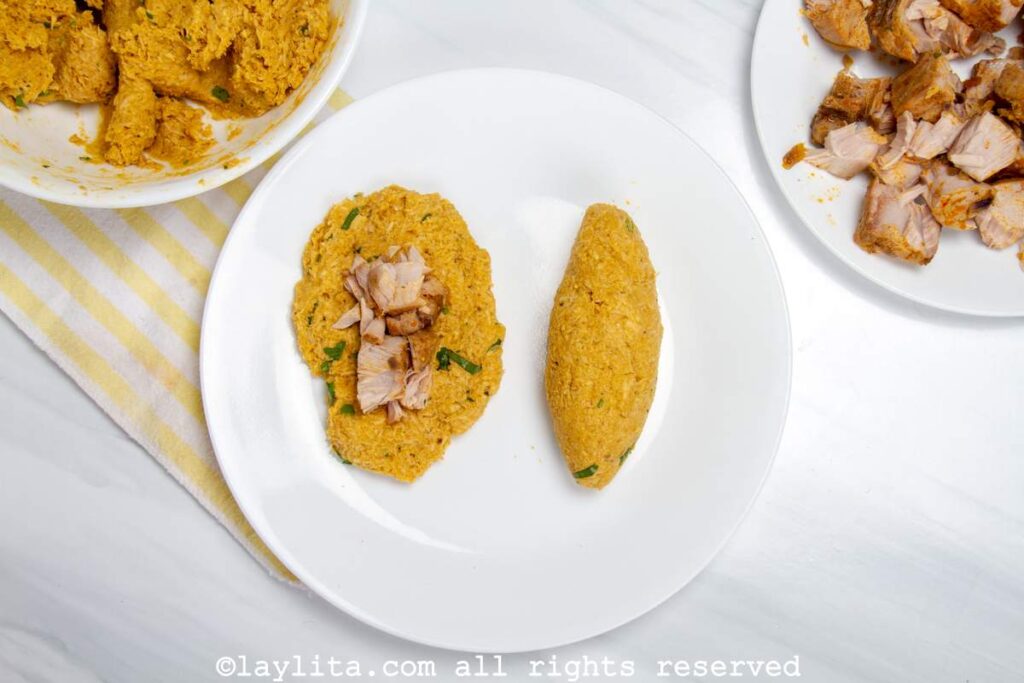 Overhead shot of an assembled corviche on a plate next to a piece of dough flattened with the pieces of fish placed in the center.