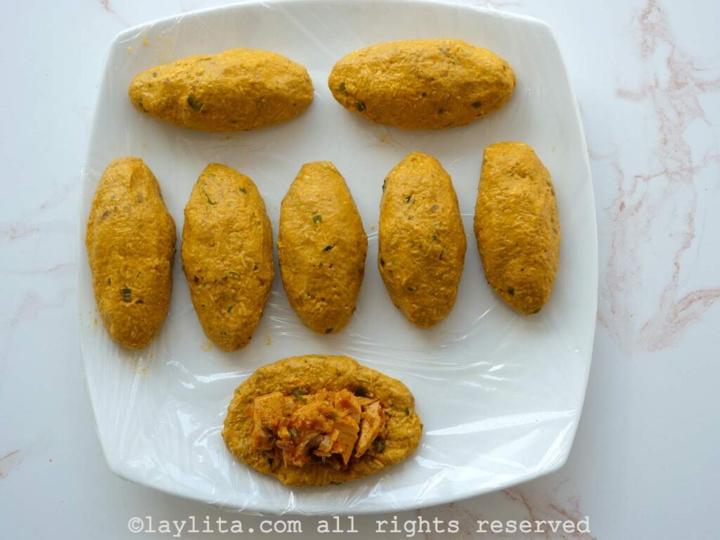 Overhead shot of an assembled corviche on a plate next to a piece of dough flattened with the pieces of fish placed in the center.