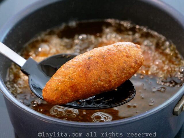 Fried corviche being taken out of a pot of oil with a spoon.