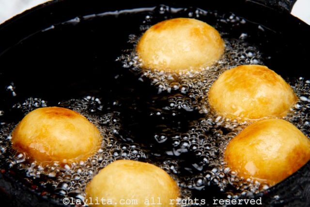 Buñuelos de yuca frying in a skillet filled with oil.