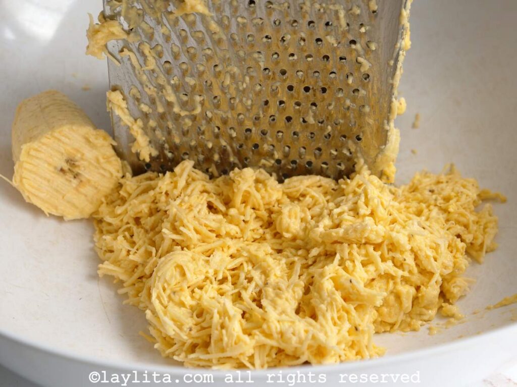 Grating green plantains with a box grater on a white plate.