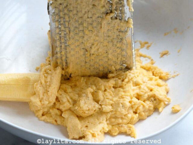 Grating green plantains with a box grater on a white plate.