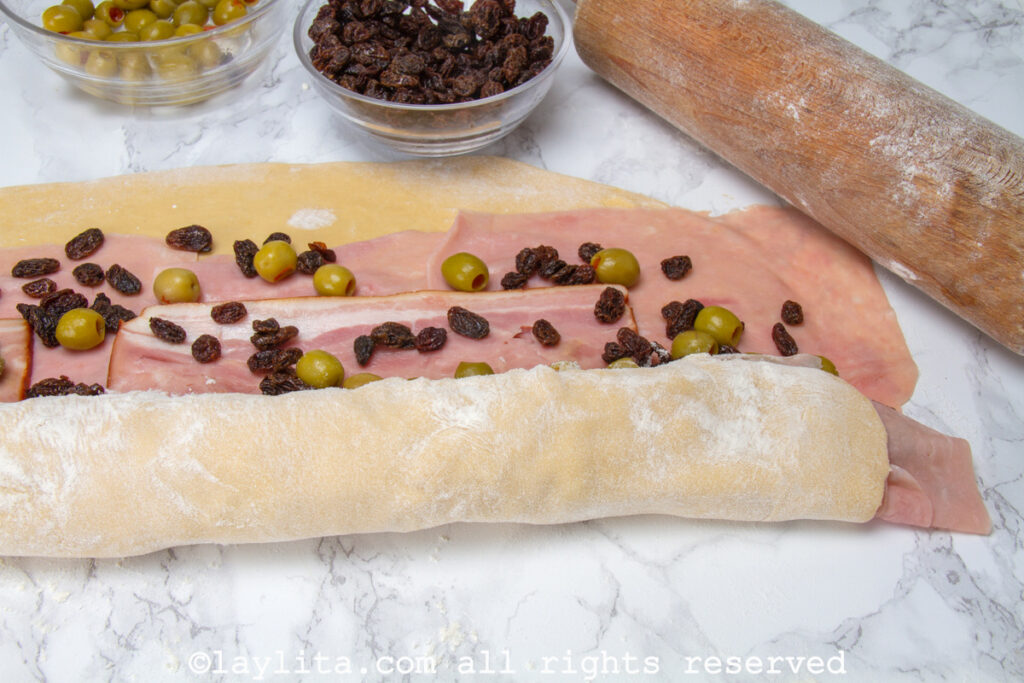 Rectangle of dough with toppings being rolled up.
