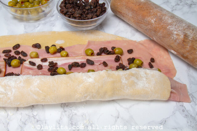 Rectangle of dough with toppings being rolled up.