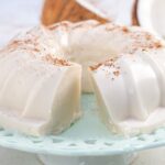 Tembleque coconut pudding served on a light blue serving platter with one slice missing and ground cinnamon on top.
