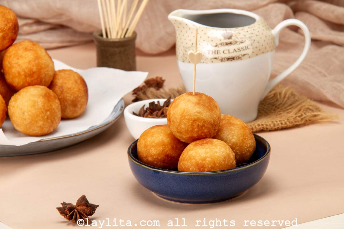 Fried buñuelos de yuca or cassava fritters served in a blue bowl with the syrup in the background.