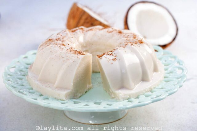 Puerto Rican Tembleque dessert on a light blue cake platter with a coconut in the background