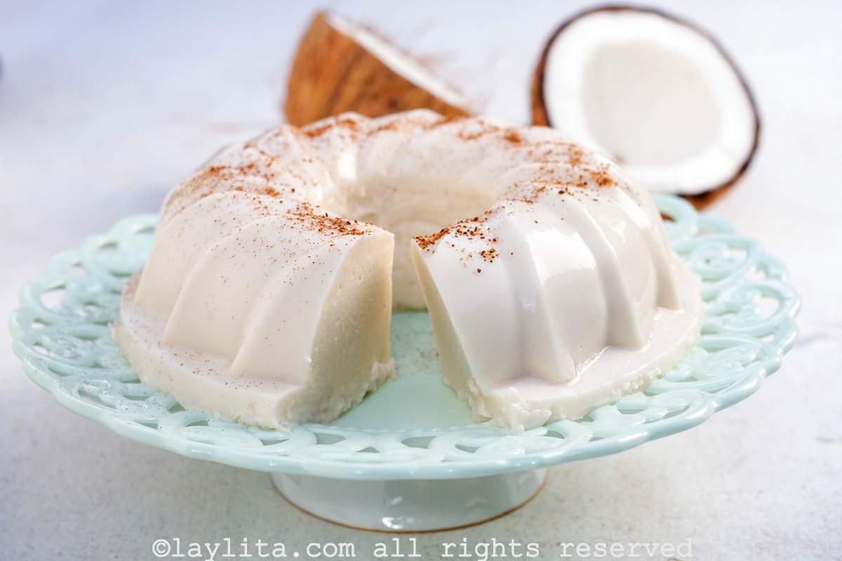 Puerto Rican Tembleque dessert on a light blue cake platter with a coconut in the background