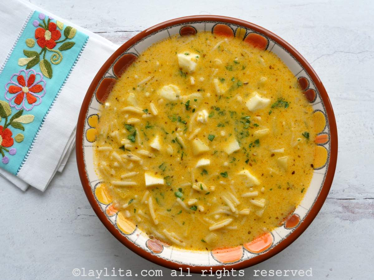 Ecuadorian sopa de fideo served in a bowl with a red rim next to an embroidered napkin.