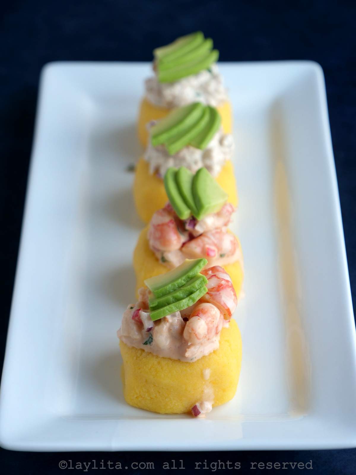 Mini Peruvian potato causa appetizer bites topped with shrimp salad and avocado on a white plate