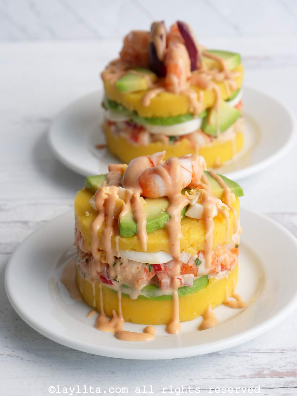 Peruvian causa de camarones topped with avocado, shrimp and pink sauce with another one in the background