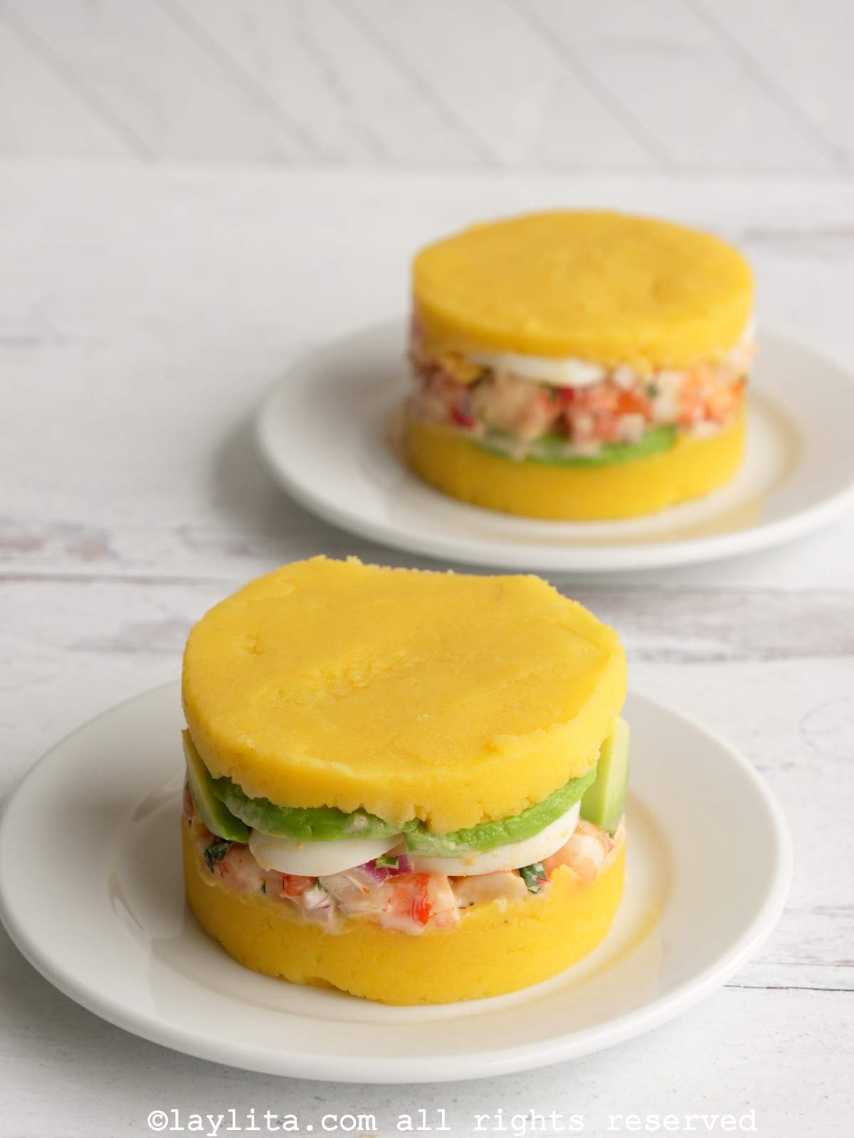 Side view of two causas served on white plates without any toppings or sauces on top.