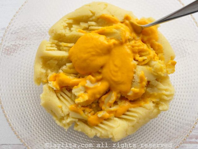 Ají amarillo paste added to the mashed potatoes in a mixing bowl.