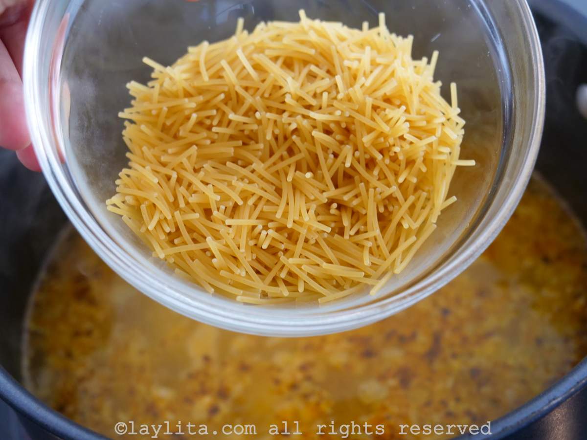 Uncooked noodles being added into the pot of soup.