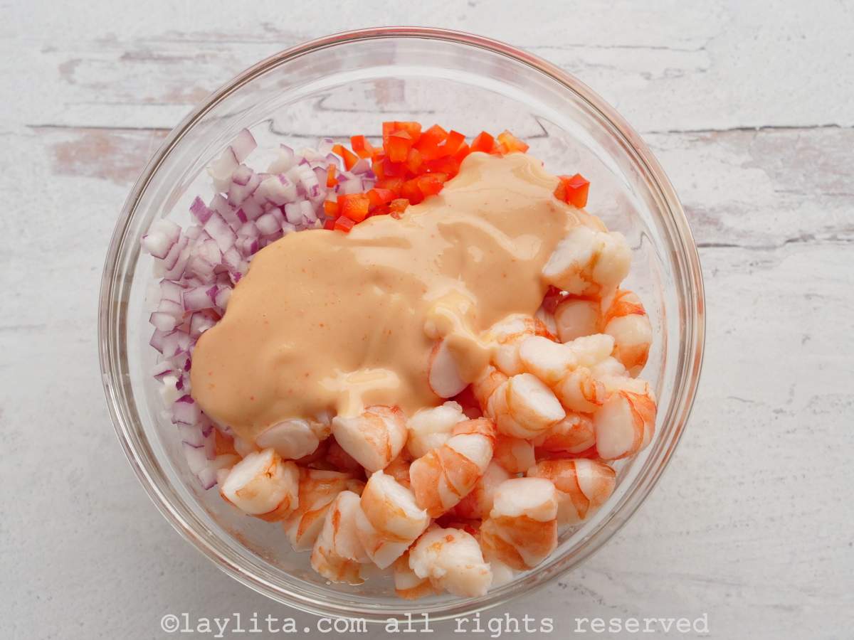 Cooked shrimp in a glass bowl with onion, pepper and pink sauce added