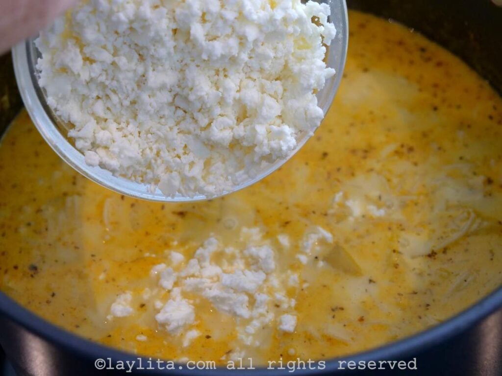 Crumbled cheese being poured into the simmering soup