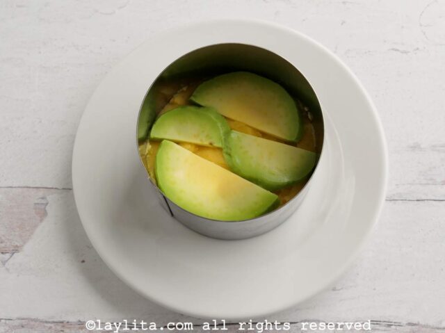 Thin avocado slices on top of a layer of potatoes in a circular mold.