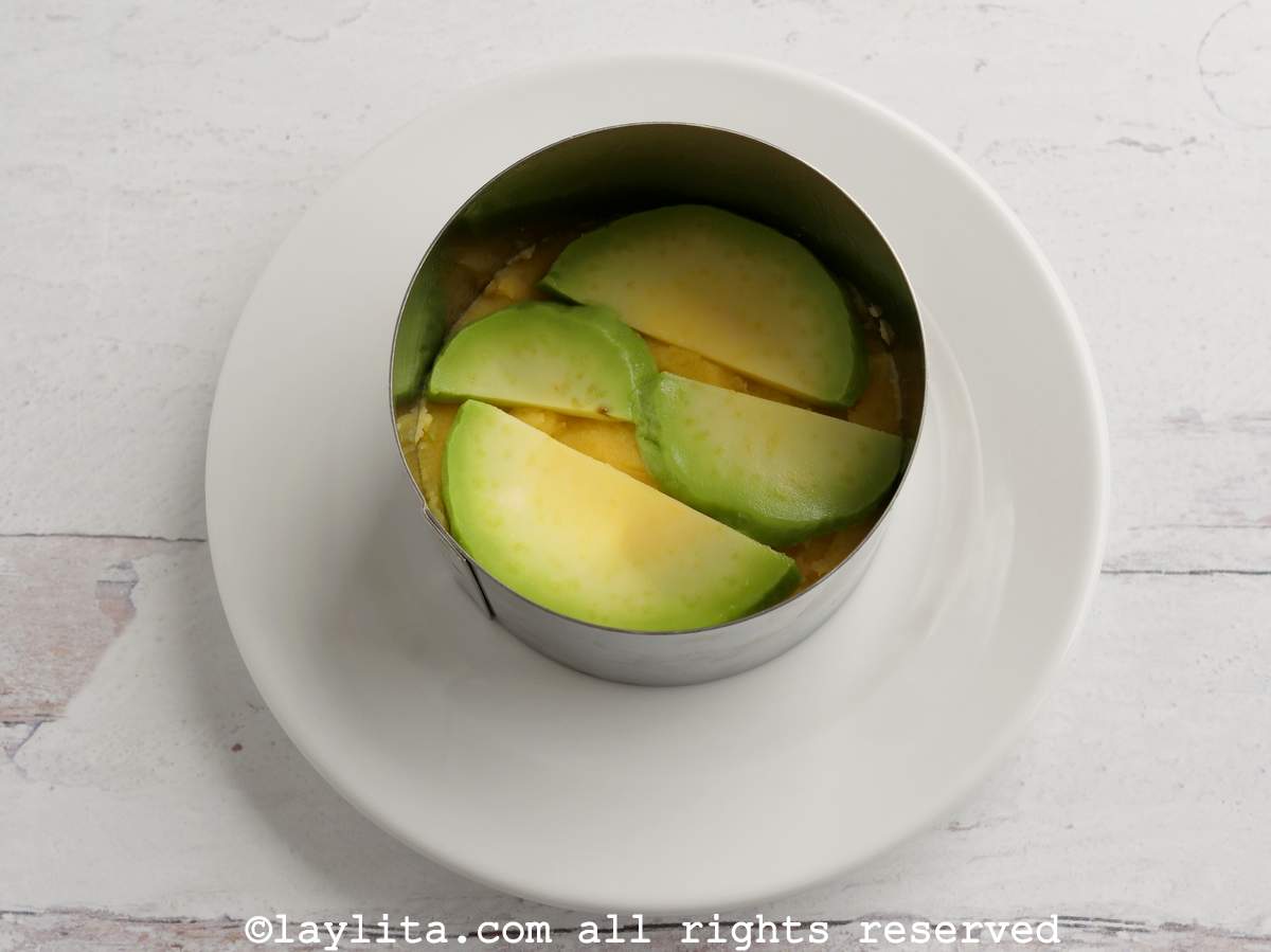Thin avocado slices on top of a layer of potatoes in a circular mold.