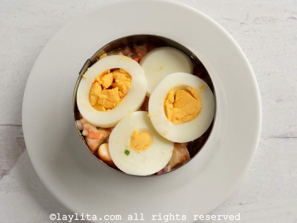 Thinly sliced boiled eggs on top of the shrimp salad in a mold.