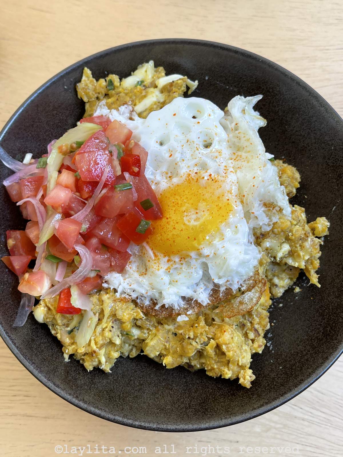 Ecuadorian green plantain tigrillo served with a fried egg and tomato salad in a black bowl