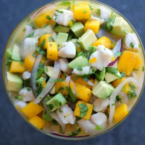Fish ceviche with mango and avocado in a glass serving bowl with a blue background