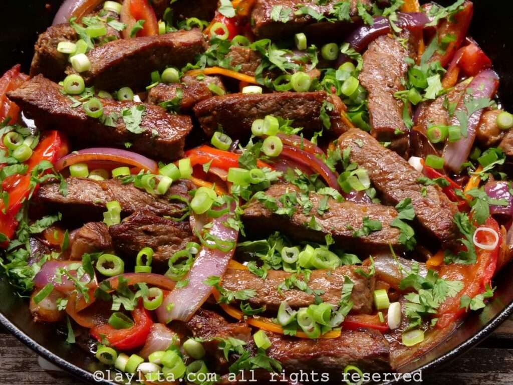 Lomo saltado in a cast iron skillet after it is done cooking with scallions and cilantro on top.