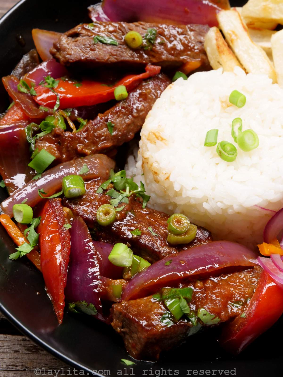 Shot of the lomo saltado stir fry on the side of a plate served with rice and fries.